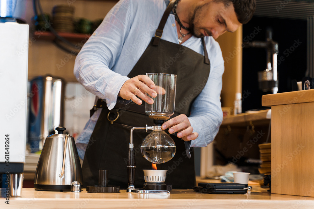 Handsome bearded barista holds Syphon device in hands before coffee brewing in cafe. Syphon alternative method of making coffee. Scandinavian method of coffee making.