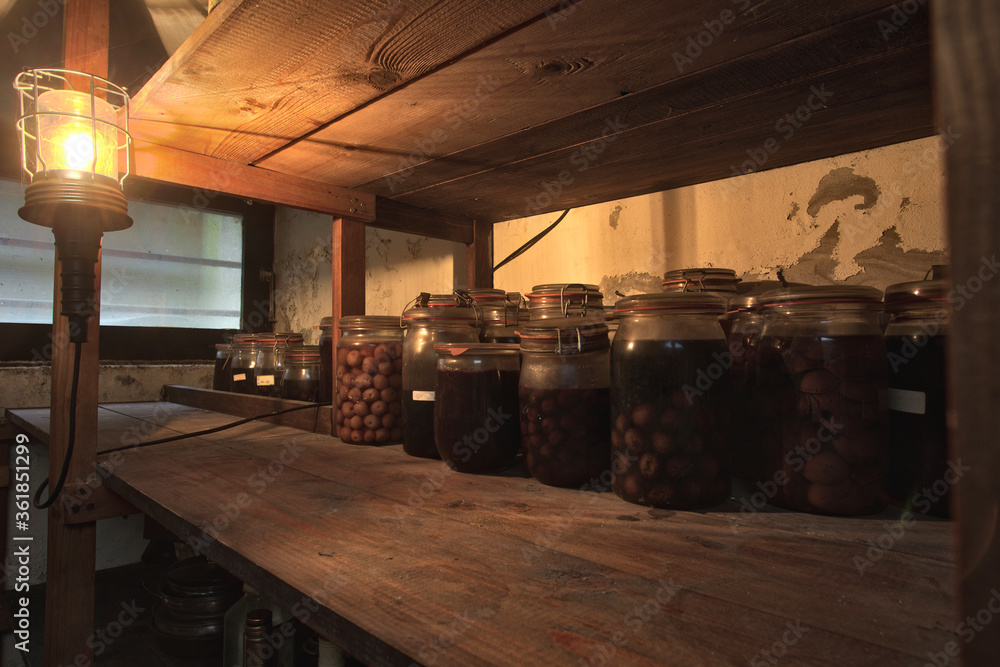 Jars with pickled vegetables, fruity compotes and jams in abandoned basement with a light hanging Preserved food in a dark cellar Jars with pickled vegetables, fruity compotes and jams in abandoned basement with a light hanging Preserved food in a dark cellar