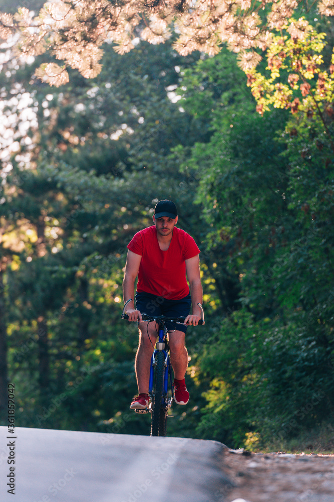 Tall handsome biker rides his bicycle on sunset in a lovely magical forest. Tall handsome biker rides his bicycle on sunset in a lovely magical forest.