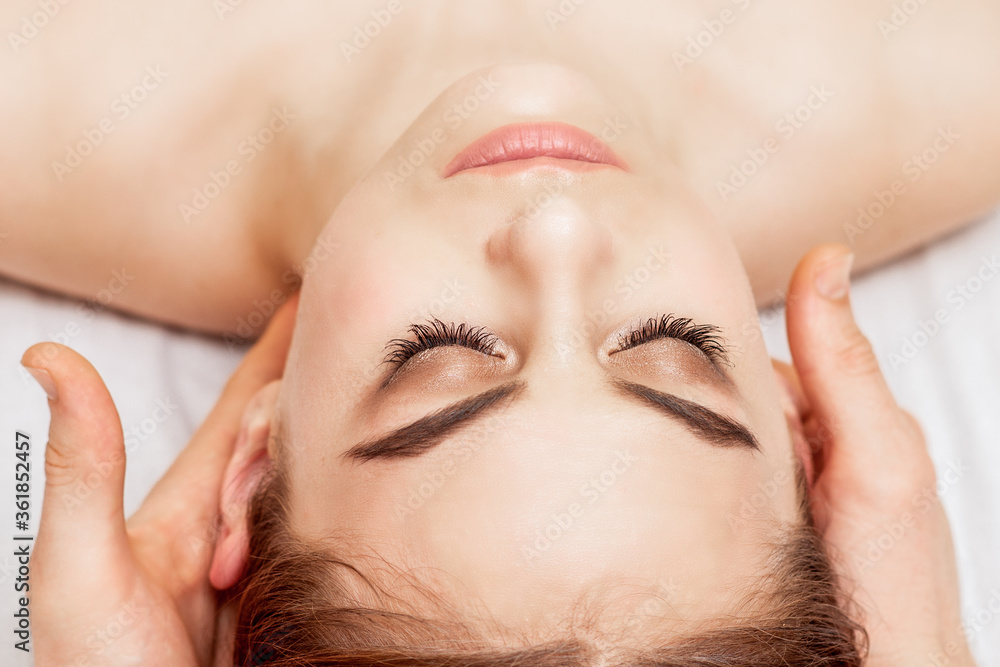 Massage therapist's hands are putting massage stones on eyes of young woman during eye massage.