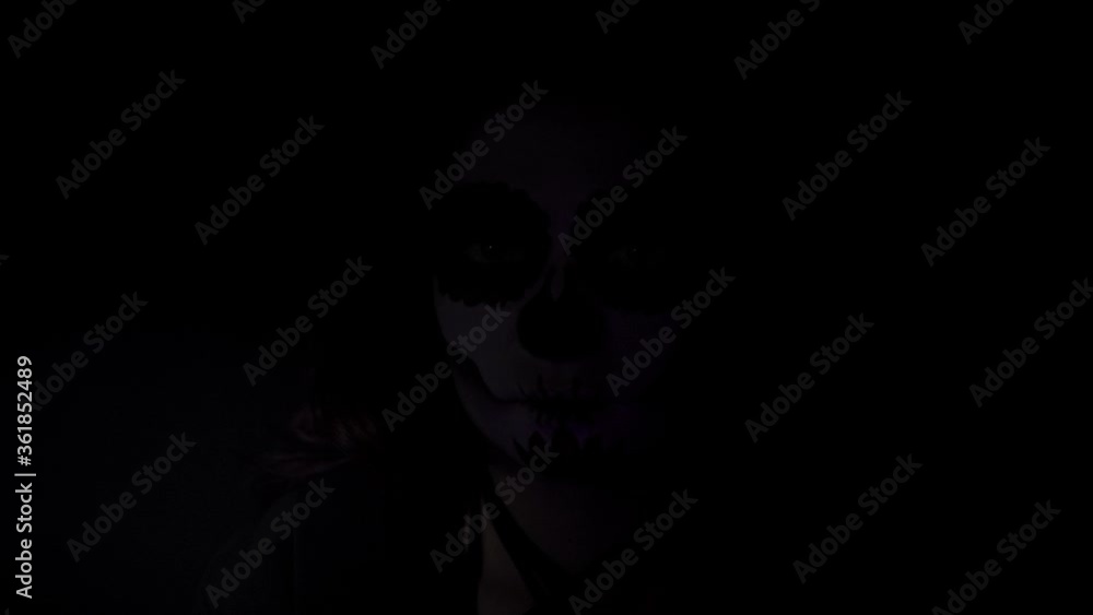 Portrait of a girl with traditional Santa Muerte makeup in a dynamic spotlight. Theme of costumes and transformation for holiday of Halloween. Standard skull makeup for day of the dead celebration Portrait of a girl with traditional Santa Muerte makeup in a dynamic spotlight. Theme of costumes and transformation for holiday of Halloween. Standard skull makeup for day of the dead celebration