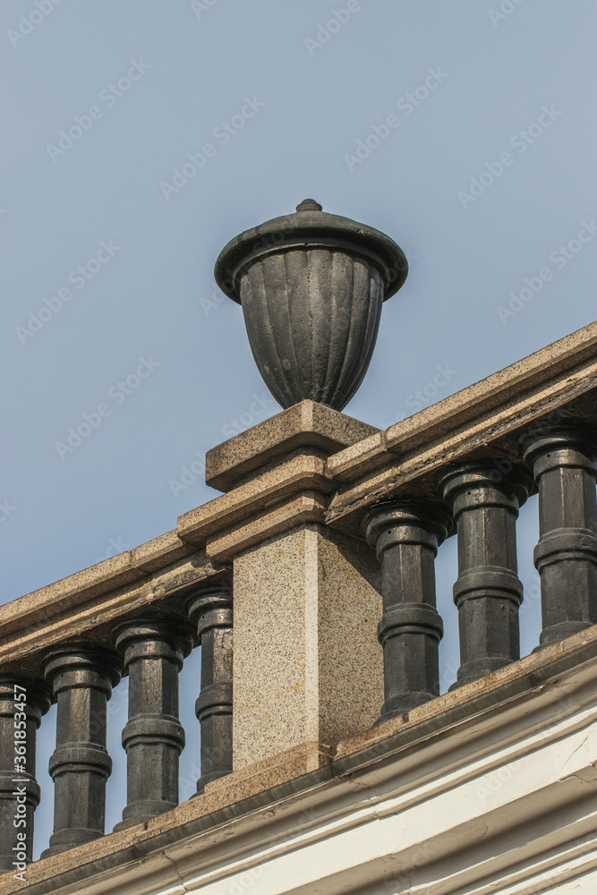 Part of a decorative building with columns and flowerpots in a city park. Walk around the city on a sunny summer day.
