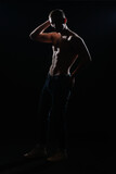 High contrast silhouette portrait of a sexy young male model shirtless posing on the side.
