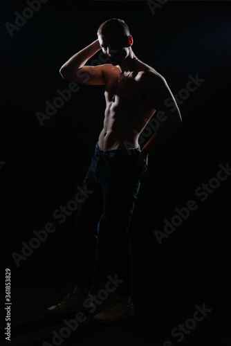 High contrast silhouette portrait of a sexy young male model shirtless posing on the side. © qunica.com