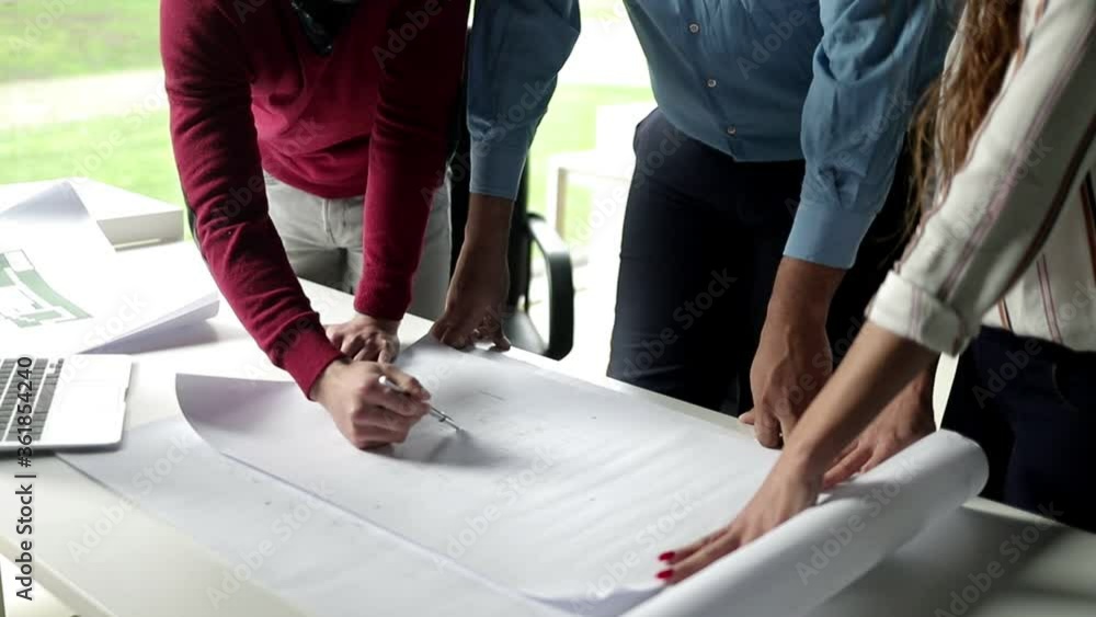 Construction expert explaining blueprint details to customers. Business people standing at table and discussing building floor plan. Cropped shot. Engineering or teamwork concept Construction expert explaining blueprint details to customers. Business people standing at table and discussing building floor plan. Cropped shot. Engineering or teamwork concept