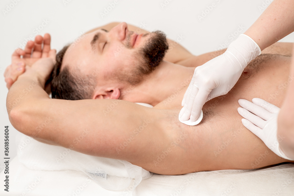 Hands of depilation master in white rubber gloves wiping male armpit with a cotton pad Hands of depilation master in white rubber gloves wiping male armpit with a cotton pad