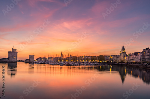 Panoramic view of the old harbor of La Rochelle at sunset with its famous old towers. beautiful orange sky