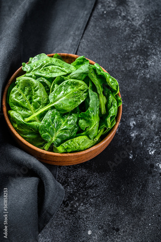 Fresh spinach leaves in a wooden bowl. Black background. Top view