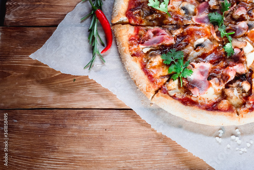 Appetizing pizza on a wooden table surrounded by herbs and spices. The concept of delicious food, restaurants and cafes