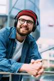 Closeup vertical portrait of happy cheerful bearded handsome male hipster enjoying music in headphones in the city
