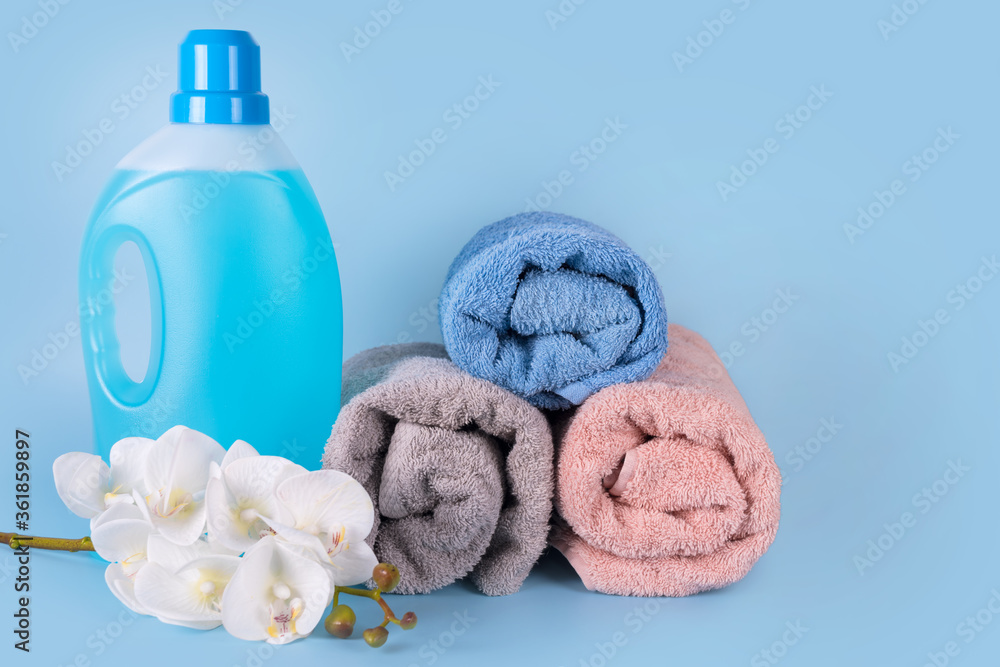 Bottle of detergent with clean towels and flowers on blue background. Plastic container of cleaning product, household chemicals, liquid laundry detergent. Laundry day, cleaning concept. Copyspace Bottle of detergent with clean towels and flowers on blue background. Plastic container of cleaning product, household chemicals, liquid laundry detergent. Laundry day, cleaning concept. Copyspace