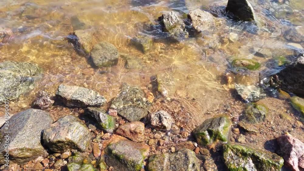 Stones in transparent water close up. sea waves approaching the rocky shore. water surface with ripples Stones in transparent water close up. sea waves approaching the rocky shore. water surface with ripples
