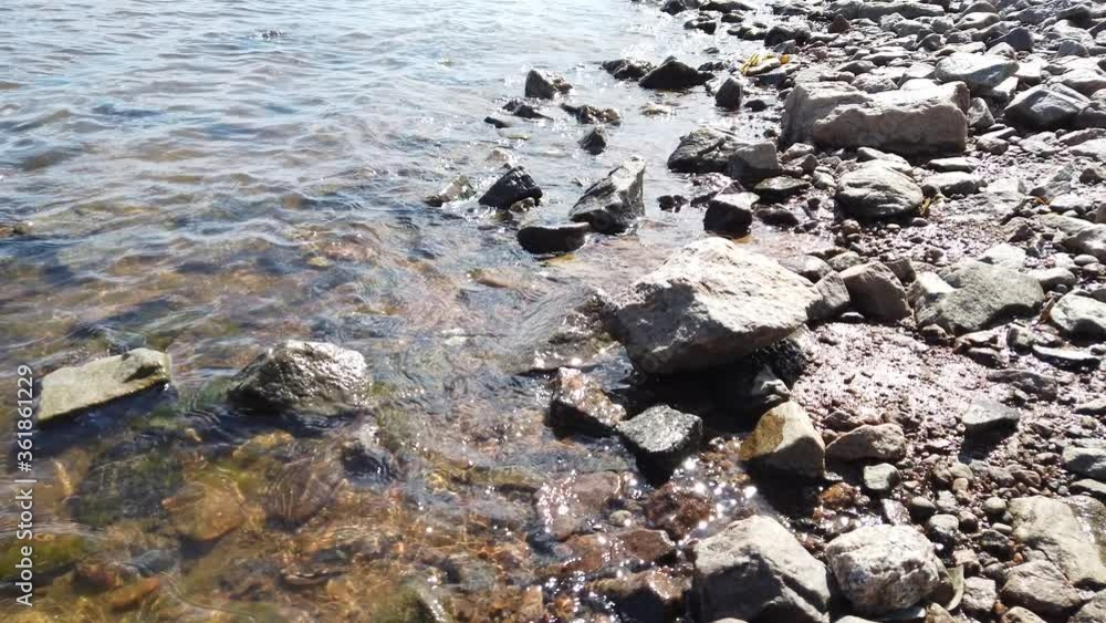 Stones in transparent water close up. sea waves approaching the rocky shore. water surface with ripples Stones in transparent water close up. sea waves approaching the rocky shore. water surface with ripples
