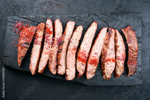 Traditional barbecue sliced dry aged wagyu flank steak offered with chili powder as overhead view on a rustic charred wooden cutting board