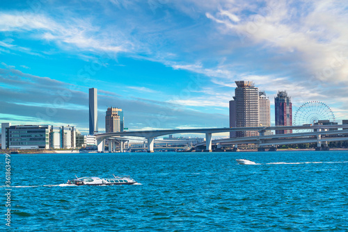 Water buses sailing on Tokyo Bay in front of the double-layered expressway of Rainbow Bridge with the buildings and ferris wheel of Odaiba and Ariake islands in the back. photo