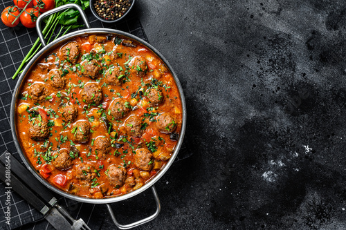 Pork meatballs with tomato sauce and vegetables in a pan. Black background. Top view. Space for text