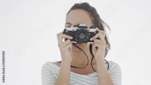 4K portrait of young beautiful woman with one eye closed and camera in hands taking pictures of viewer and smiling slighly. photo