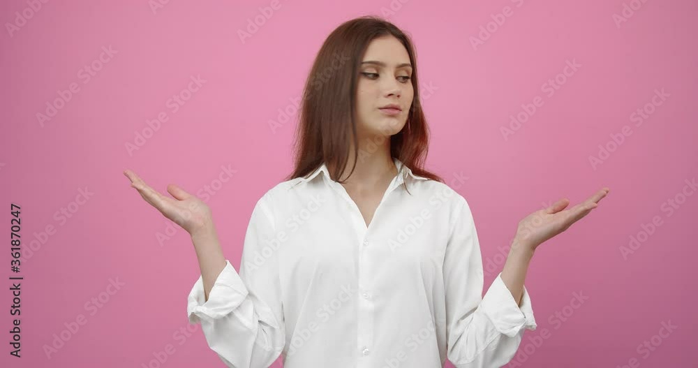Charming young girl in white shirt holding hands with open palms and feeling confused because of choice she needs to make. Isolated over pink background. Space for text and advertisement. Charming young girl in white shirt holding hands with open palms and feeling confused because of choice she needs to make. Isolated over pink background. Space for text and advertisement.