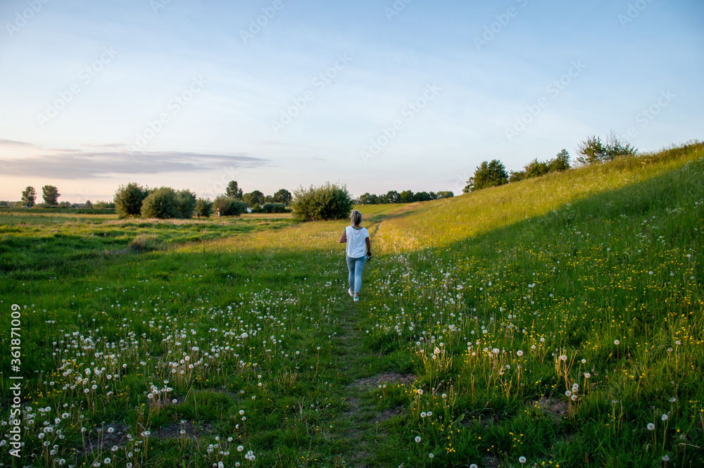 Caucasian woman with long blond hair walking through a typical Dutch green meadow with flowers and while the sun is setting Caucasian woman with long blond hair walking through a typical Dutch green meadow with flowers and while the sun is setting