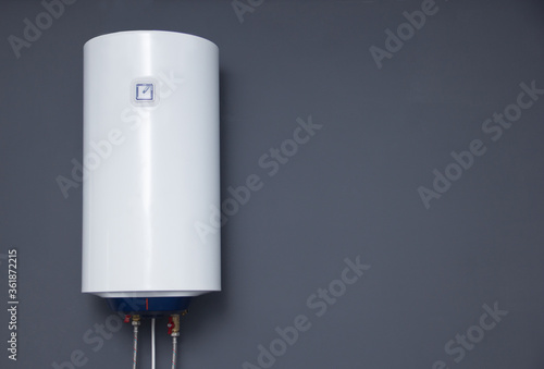 Modern electric boiler on a gray plain wall. White water heater. Space for text photo