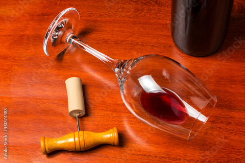 Принти на полотні An overturned glass of wine with a little red wine next to a corkscrew and a bottle on a wooden bottom