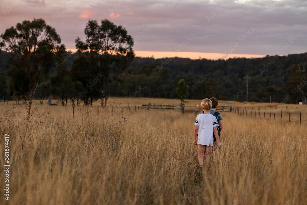 Young boys walking through field at sunset Young boys walking through field at sunset
