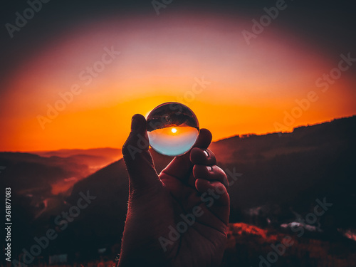 Taking photos of sunset through the small glass ball holding in hand