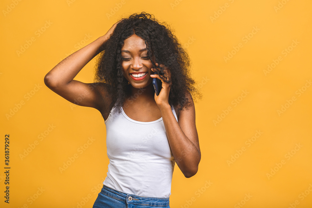 Portrait of a cute happy afro american black girl in casual talking on mobile phone and laughing isolated over yellow background. Portrait of a cute happy afro american black girl in casual talking on mobile phone and laughing isolated over yellow background.