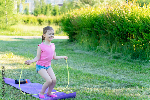 The child goes in for sports in the park. Girl jumping rope