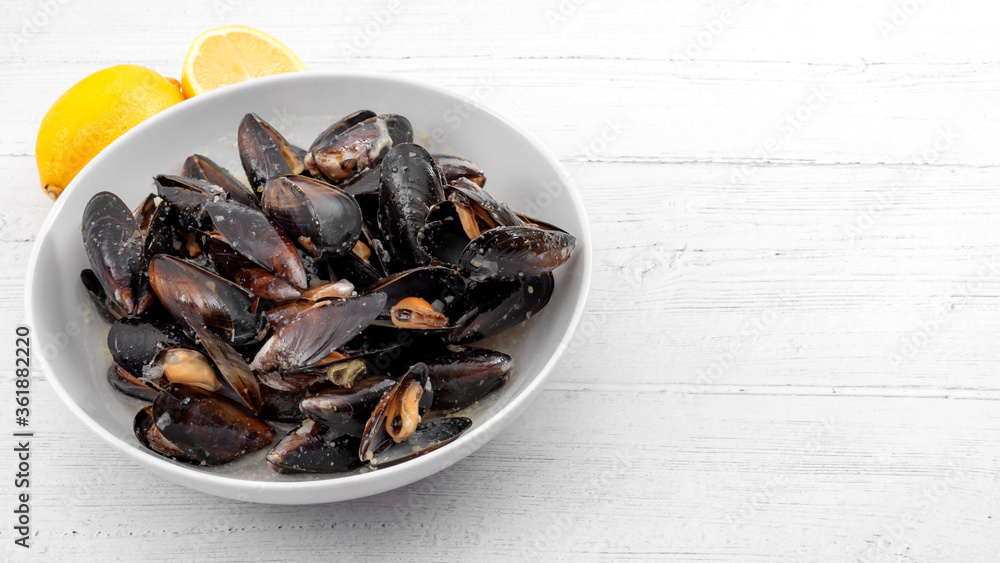 Protein and zinc rich sea food, marine delicacy and luxury foods concept with photograph of a bowl of raw mussels and lemons isolated on rustic white wood background with copy space Protein and zinc rich sea food, marine delicacy and luxury foods concept with photograph of a bowl of raw mussels and lemons isolated on rustic white wood background with copy space