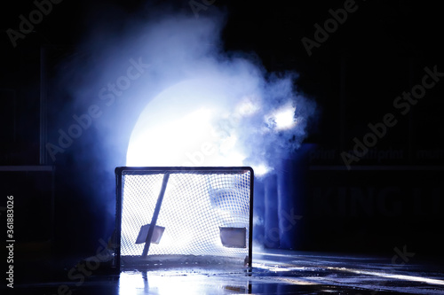 Canvas Print An ice hockey goal standing in the shadow in front of the player entrance with bright light and smoke coming out