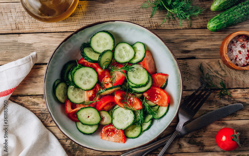 Healthy vegetable salad of fresh tomato, cucumber, dill and spices and oil in bowl on rustic wooden background. Diet concept.