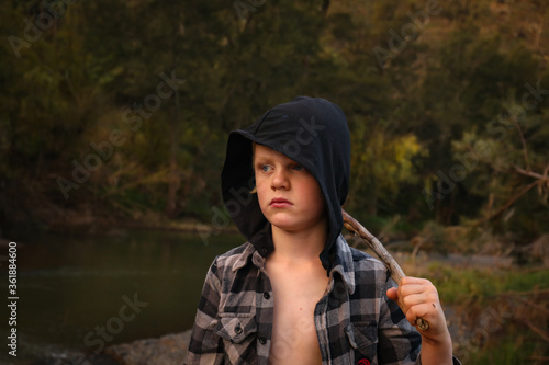 Little boy wearing hoodie playing in nature at dusk with large stick