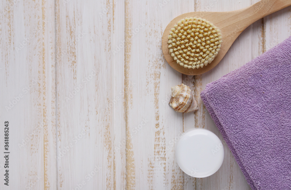 A wooden brush for dry anti-cellulite massage, a seashell, a jar of moisturizer and a folded lilac towel on a white wooden background. Spa. Selective focus. The view from the top. Keyboard layout A wooden brush for dry anti-cellulite massage, a seashell, a jar of moisturizer and a folded lilac towel on a white wooden background. Spa. Selective focus. The view from the top. Keyboard layout