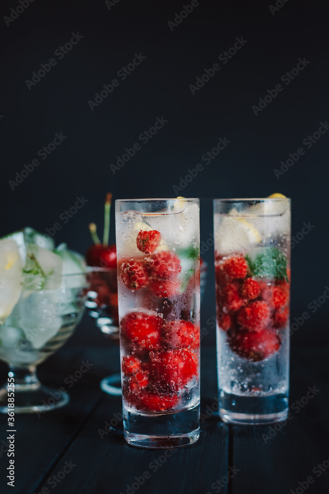 Cold lemonade with raspberries, lemon, ice and cherries on black background Cold lemonade with raspberries, lemon, ice and cherries on black background