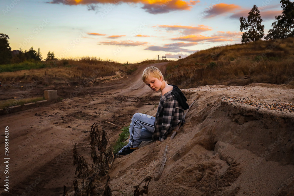 Young boy sitting on sandy bank at dusk