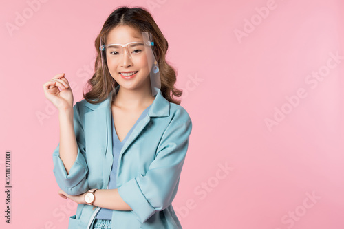 Young Asian woman posing in front of pink background with face shield on her face to protect herself from infection. © Pixpan