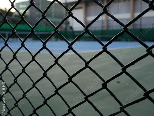 closeup of metal fence with blurred tennis court background.