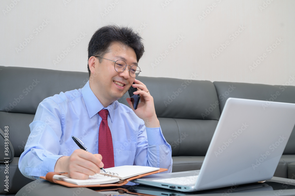 Middle-aged Asian businessman sitting on sofa in living room working at home. Telecommuting concept. Middle-aged Asian businessman sitting on sofa in living room working at home. Telecommuting concept.