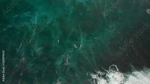 Surfers pedal out in ocean waves. seen from above. Drone aerial shot 4k. Tropical paradise, Hawaii adventure vacation, north shore big waves surf, island travel.  photo