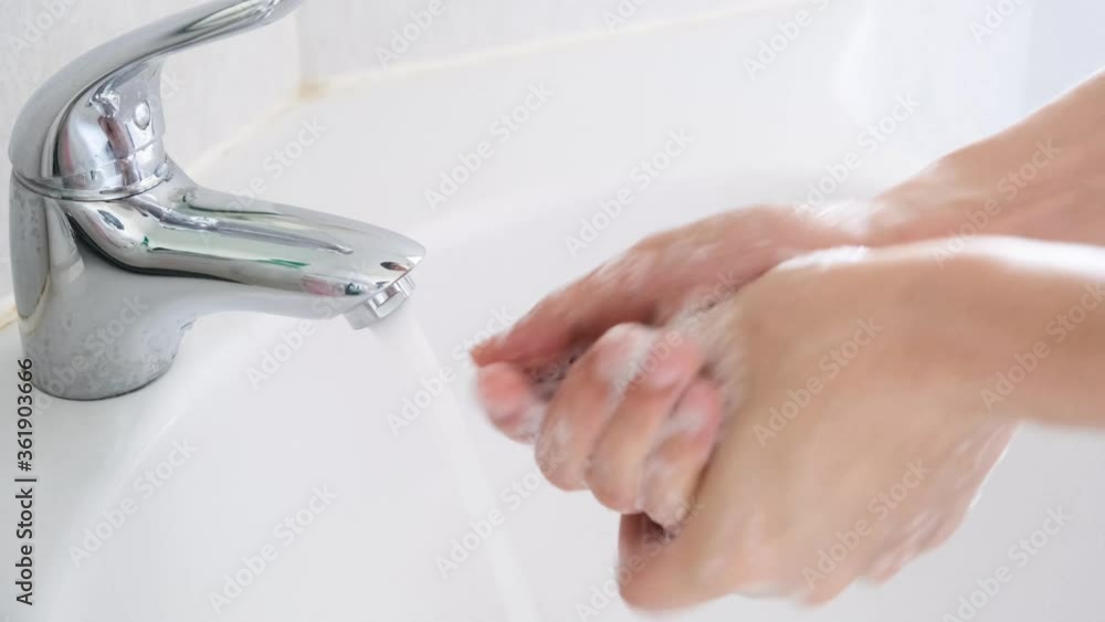 Hands of woman wash their hands in a sink with foam to wash the skin and water flows through the hands. Concept of health, cleaning and preventing germs and coronavirus from contacting hands Hands of woman wash their hands in a sink with foam to wash the skin and water flows through the hands. Concept of health, cleaning and preventing germs and coronavirus from contacting hands