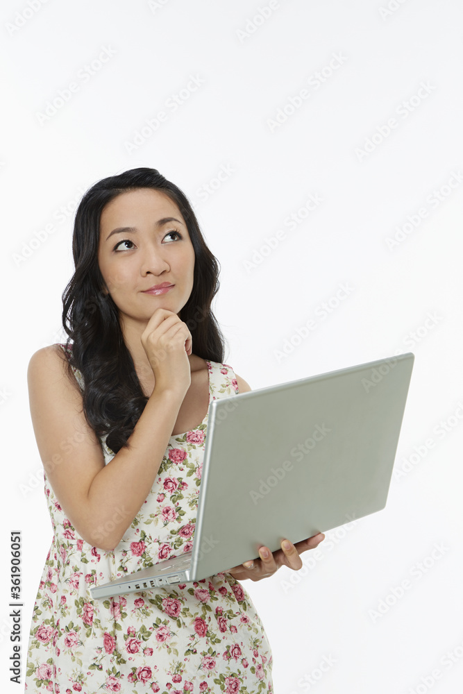Woman using a laptop while standing, contemplating Woman using a laptop while standing, contemplating
