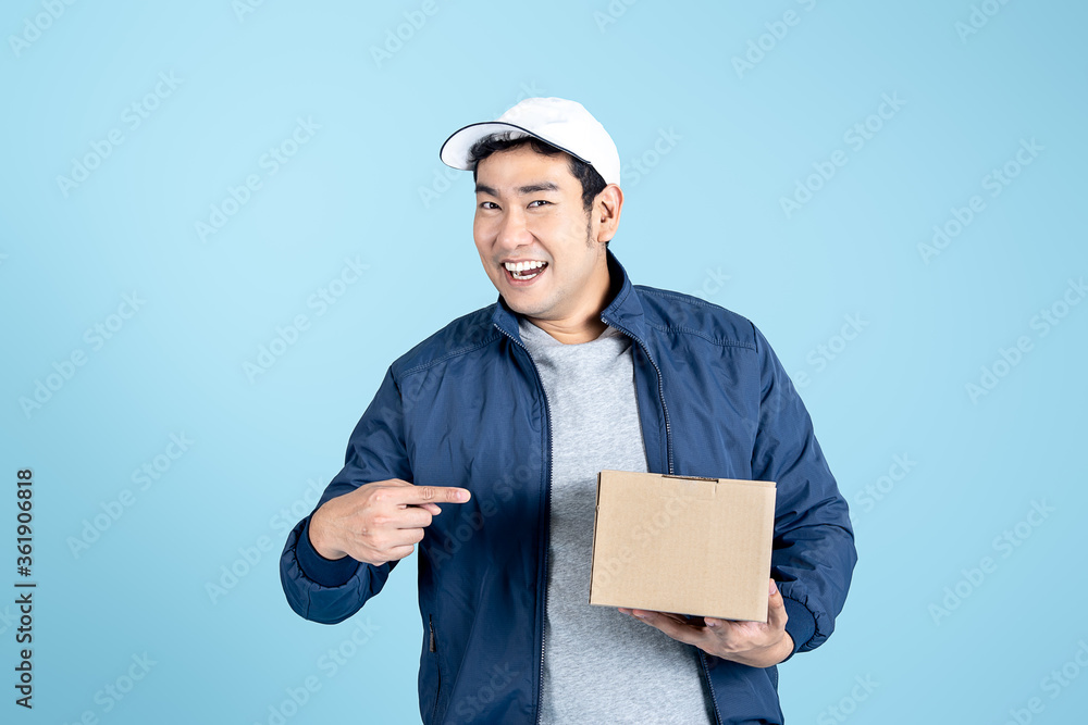 Happy Asian man from delivery service in blue jacket and cap giving food order and holding box isolated over blue background. Happy Asian man from delivery service in blue jacket and cap giving food order and holding box isolated over blue background.