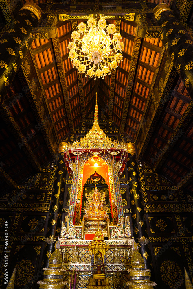 A golden Buddha stature or sculpture in the ancient wooden chapel with beautiful ceiling decoration at wat Pipat Mongkol - Sukhothai, Thailand. 