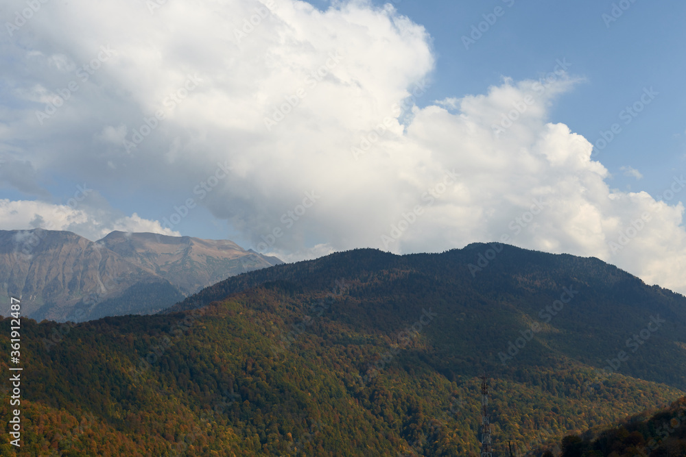 nature landscape and travel concept - mountains and trees against the blue sky with clouds in early autumn