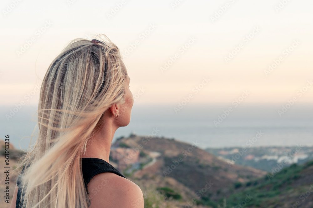 The view from the back of the head of a girl with hair fluttering in the wind with a blurred background of hills and the Mediterranean Sea, looks dreamily into the distance. The view from the back of the head of a girl with hair fluttering in the wind with a blurred background of hills and the Mediterranean Sea, looks dreamily into the distance.
