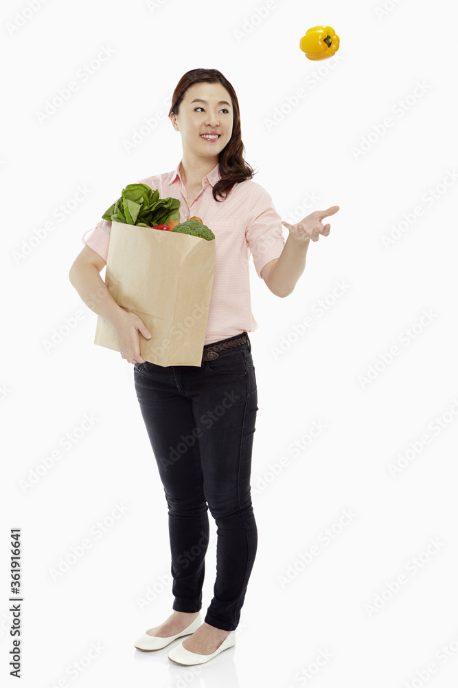 Woman with groceries tossing up a capsicum Woman with groceries tossing up a capsicum