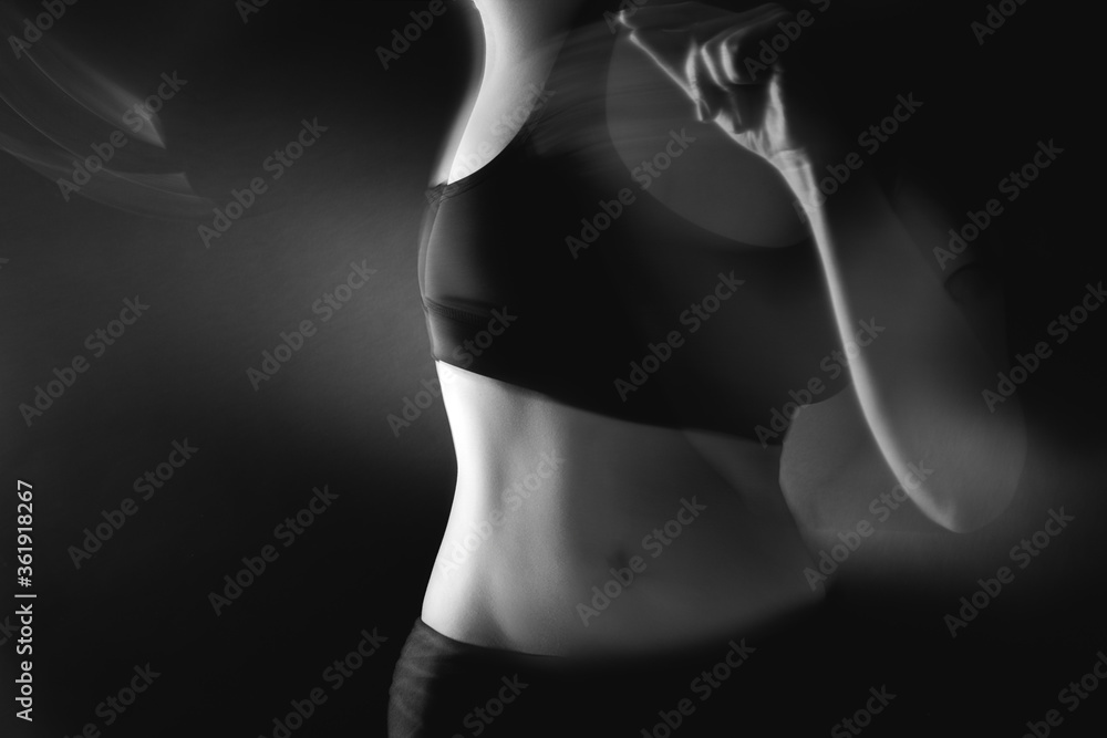 Naklejka premium Feminine energy. Body vitality. Defocused woman silhouette in black athletic top on gray background.