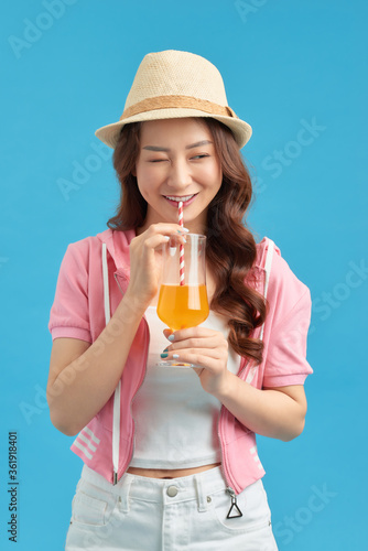 Happy Asian woman in summer casual clothes with a glass of fresh fruit juice drink on blue background