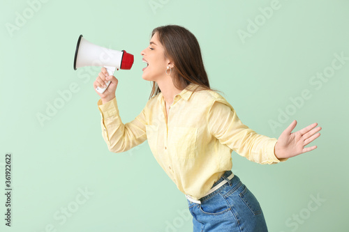 Beautiful young woman with megaphone on color background